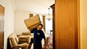Mitarbeiter trägt Sofa aus Wohnzimmer einer Wohnungsauflösung raus