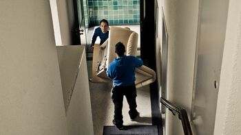 zwei Mitarbeiter tragen Sofa einer Entrümpelung oder Haushaltsauflösung ein Treppenhaus runter